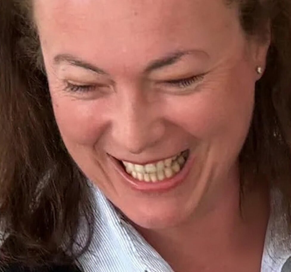 Gros plan d'une femme aux cheveux bruns et bouclés, souriant avec les yeux fermés