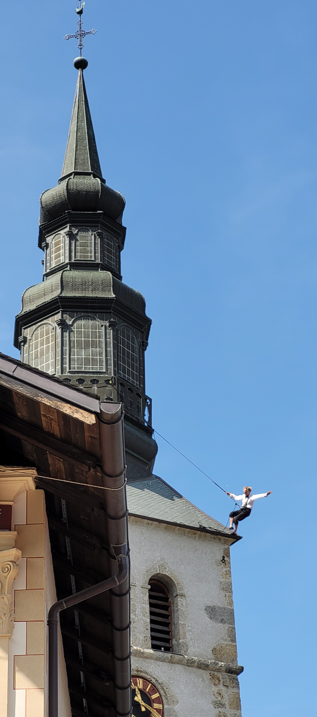 Un funambule est relié par un câble de sécurité au clocher d'une église, marchant sur le toit.